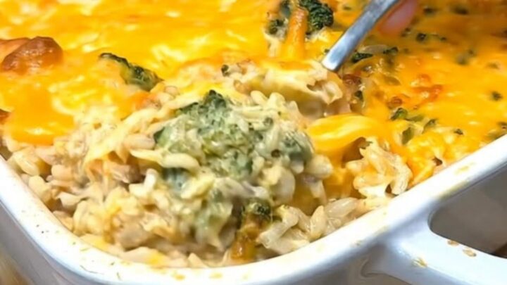 A steaming, cheesy chicken broccoli rice casserole in a white baking dish.
