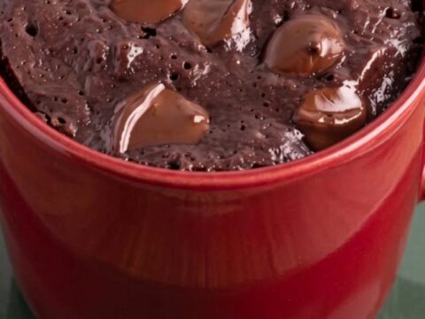 Warm chocolate mug brownie in a red ceramic mug topped with glossy melted chocolate chips.