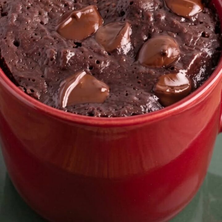 Warm chocolate mug brownie in a red ceramic mug topped with glossy melted chocolate chips.