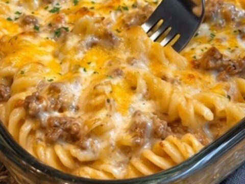 A serving of cheesy beef rotini casserole with a visible cheese pull on a white plate.
