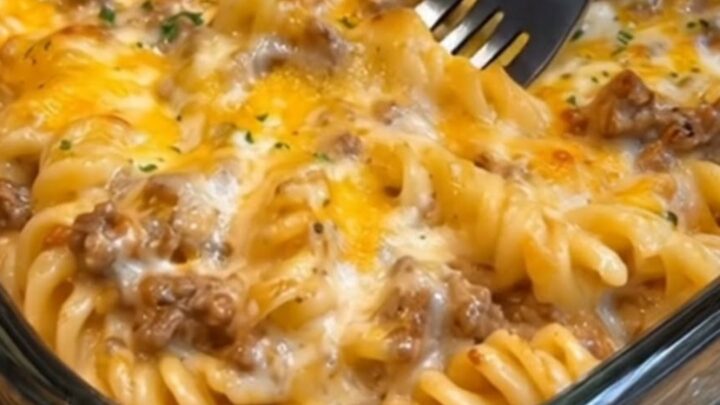 A serving of cheesy beef rotini casserole with a visible cheese pull on a white plate.