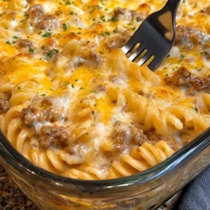 A serving of cheesy beef rotini casserole with a visible cheese pull on a white plate.
