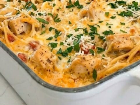 A white ceramic baking dish filled with cheesy chicken spaghetti, featuring a rich, bubbling melted cheese topping.
