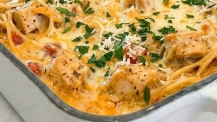 A white ceramic baking dish filled with cheesy chicken spaghetti, featuring a rich, bubbling melted cheese topping.