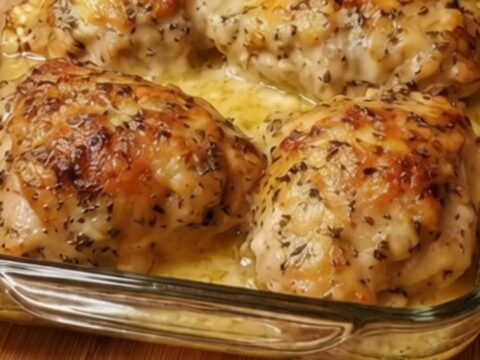 A golden, baked chicken thigh served in a creamy herb sauce inside a glass baking dish.