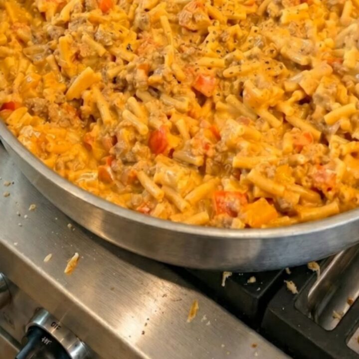 A steaming, creamy portion of cheesy taco mac in a stainless steel skillet with a stretchy cheese pull.