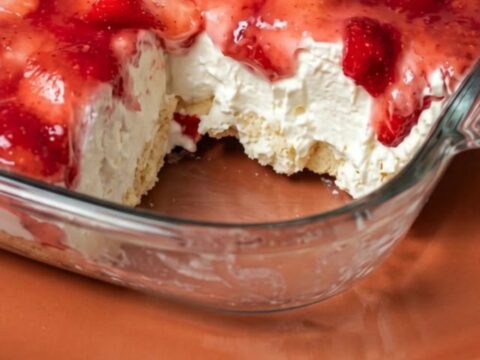 A clear glass dish filled with layers of angel food cake, creamy filling, and topped with fresh sliced strawberries.