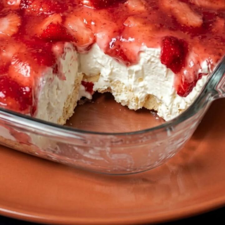 A clear glass dish filled with layers of angel food cake, creamy filling, and topped with fresh sliced strawberries.