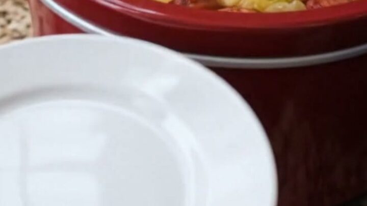 A steaming red slow cooker filled with sliced smoked sausage, tender cabbage, and cubed potatoes.