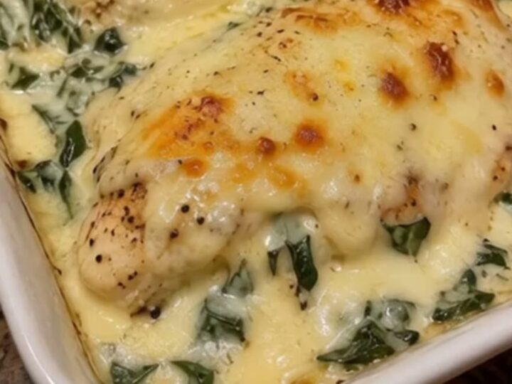 A golden, bubbling cheesy chicken breast in a white baking dish with creamy spinach.