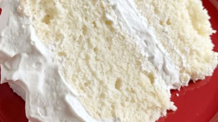 A tall slice of fluffy white layer cake with smooth frosting on a white cake stand.