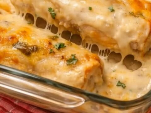 A close-up of a cheesy white chicken enchilada being lifted from a glass dish with a wooden spatula.