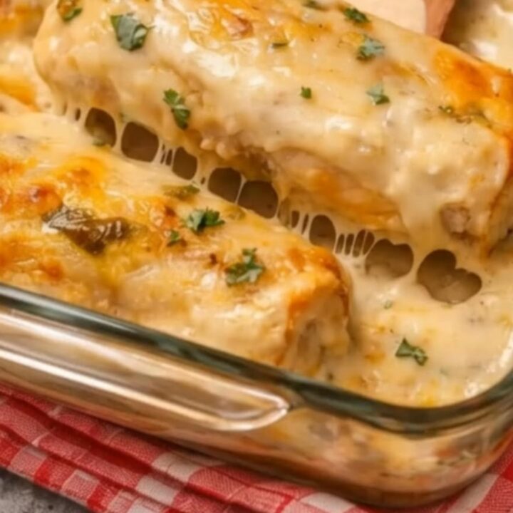 A close-up of a cheesy white chicken enchilada being lifted from a glass dish with a wooden spatula.