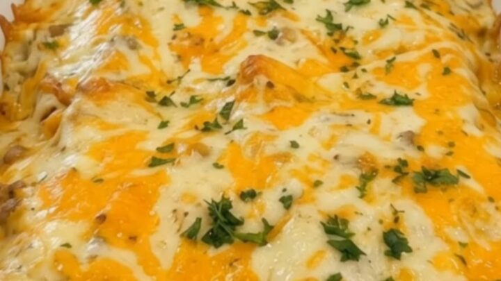 A white baking dish filled with golden, cheesy sausage and gravy enchiladas, garnished with fresh parsley.