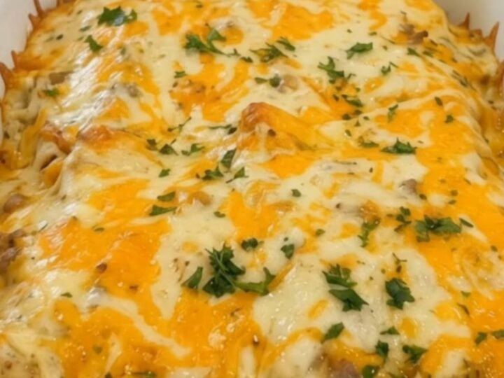 A white baking dish filled with golden, cheesy sausage and gravy enchiladas, garnished with fresh parsley.