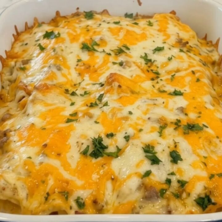 A white baking dish filled with golden, cheesy sausage and gravy enchiladas, garnished with fresh parsley.