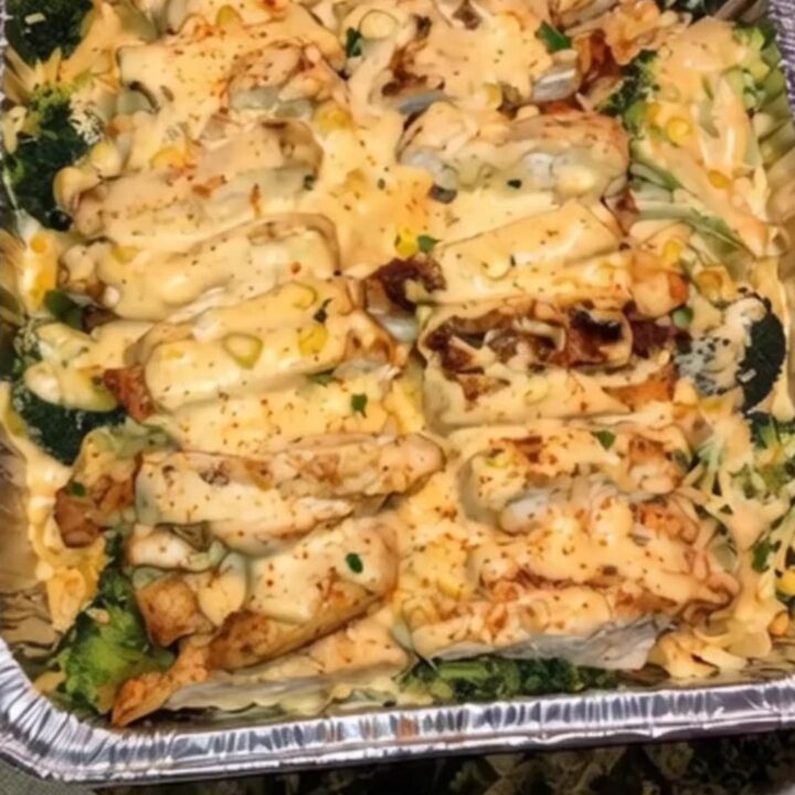 A steaming, creamy chicken and broccoli casserole in a foil baking dish, showing melted cheese and tender pieces of chicken.