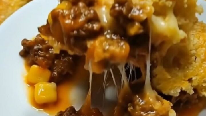 A warm, golden-brown cheesy cowboy cornbread casserole in a white baking dish with steam rising.