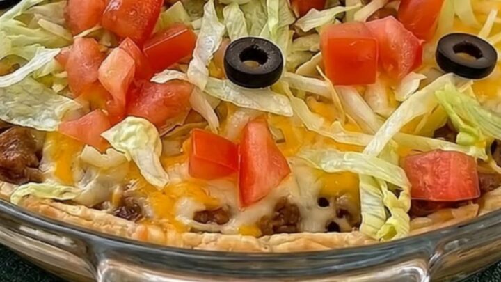 A freshly baked golden taco pie in a glass dish on a green runner.