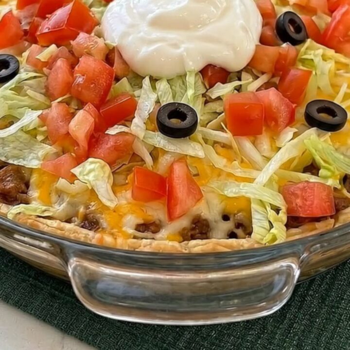A freshly baked golden taco pie in a glass dish on a green runner.