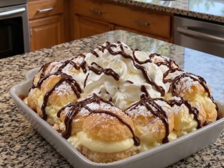 A decadent cream puff cake in a ceramic dish, topped with whipped cream and chocolate drizzle.