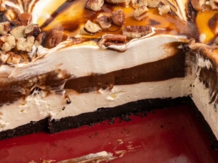 A red ceramic baking dish filled with layered sugar-free turtle lush topped with caramel and pecans.