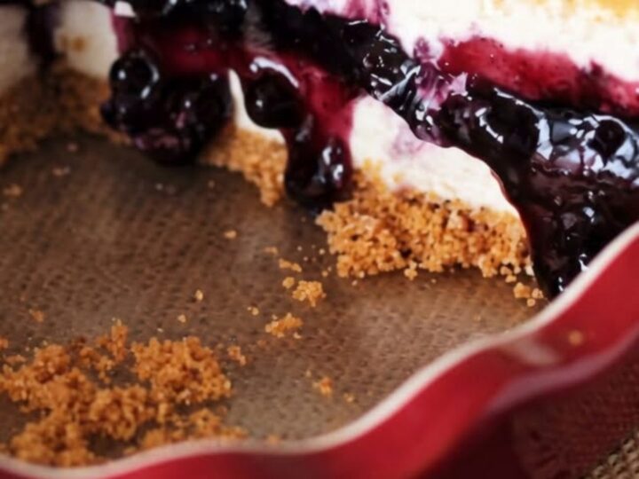 A slice of no-bake blueberry cheesecake pie on a white plate with a fork resting nearby.