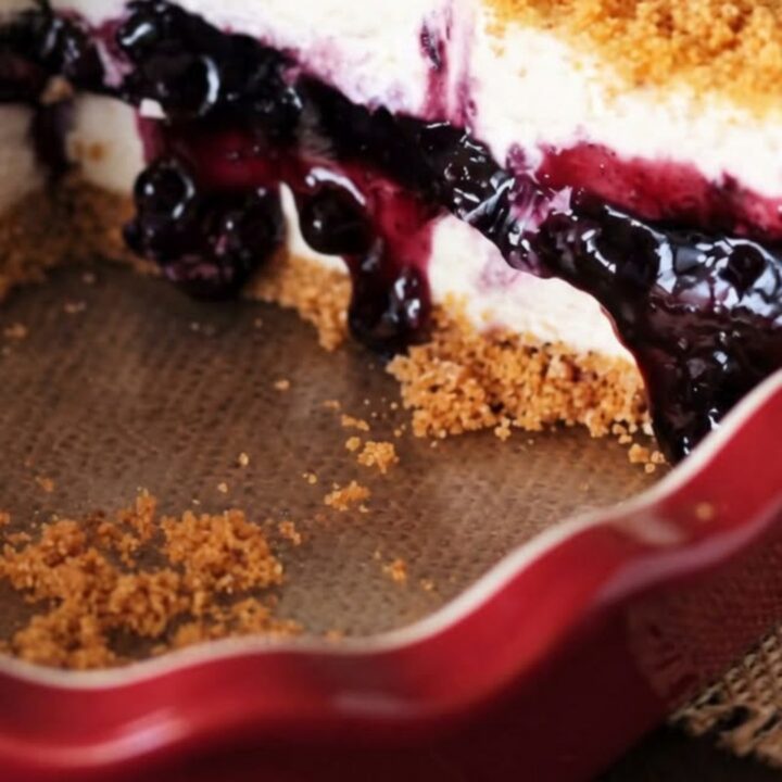 A slice of no-bake blueberry cheesecake pie on a white plate with a fork resting nearby.