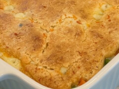 A golden-brown chicken cobbler in a white fluted baking dish, with a portion being scooped out to reveal a creamy filling.