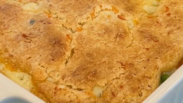 A golden-brown chicken cobbler in a white fluted baking dish, with a portion being scooped out to reveal a creamy filling.