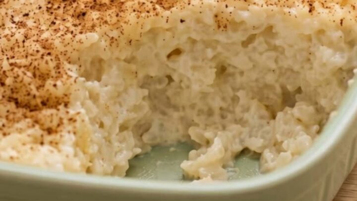 A ceramic dish filled with creamy baked rice pudding, dusted with cinnamon, ready to be served.