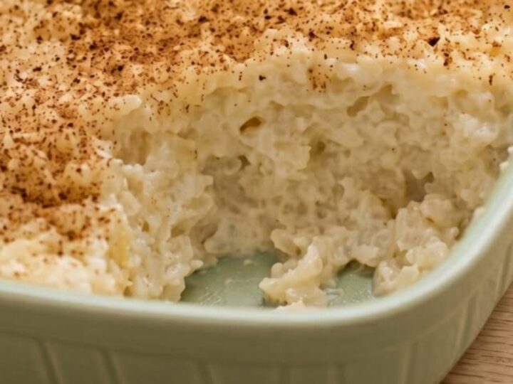 A ceramic dish filled with creamy baked rice pudding, dusted with cinnamon, ready to be served.