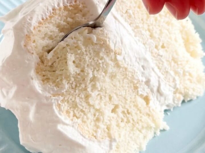 A thick, fluffy slice of sugar-free white cake on a cake stand with pillowy white frosting.