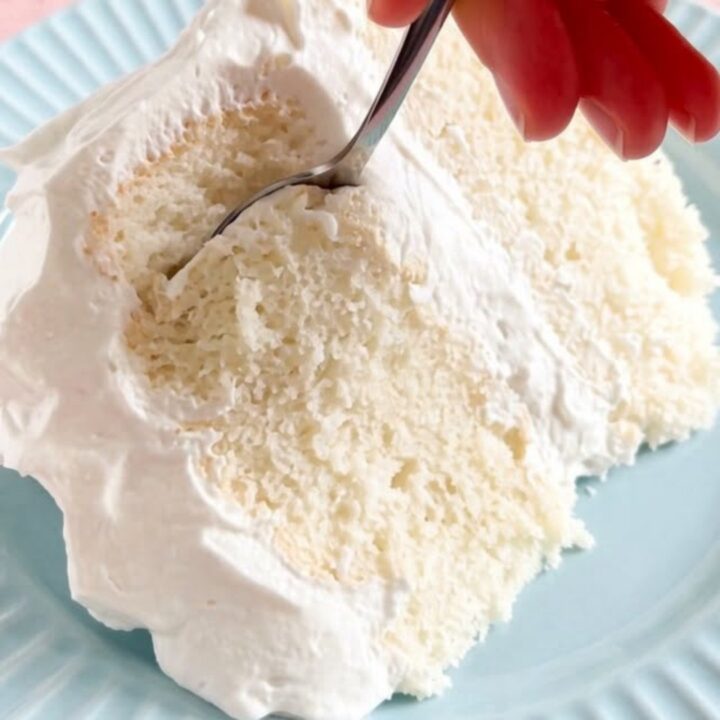 A thick, fluffy slice of sugar-free white cake on a cake stand with pillowy white frosting.