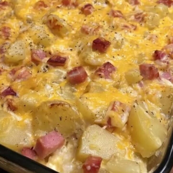 A serving spoon scooping a portion of hot cheesy ham and potato casserole with an elastic cheese pull.