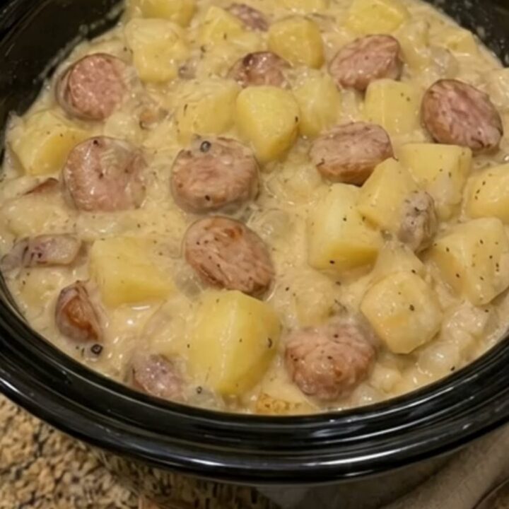 A close-up of a white bowl filled with creamy diced potatoes and sliced smoked sausage, steaming hot.