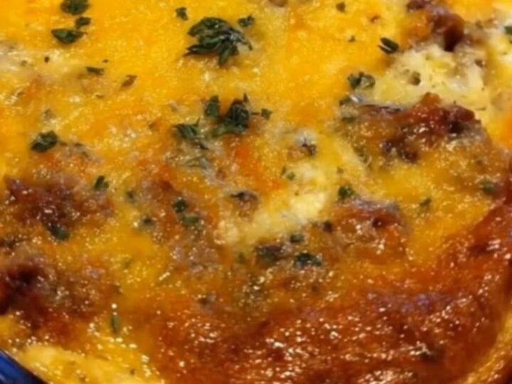 A golden, bubbly breakfast casserole in a glass dish with melted cheese and fresh herbs on top.