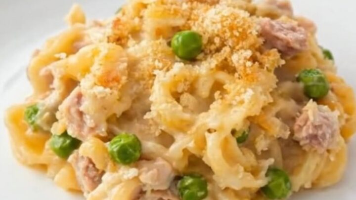 A steaming portion of creamy tuna casserole with peas and golden breadcrumbs in a glass baking dish.