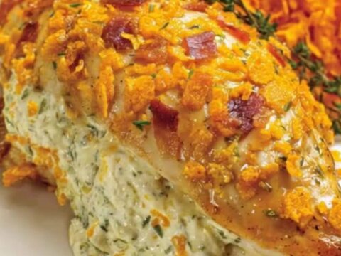 A golden, bacon-wrapped stuffed chicken breast with a crunchy crust in a baking dish, with visible steam.