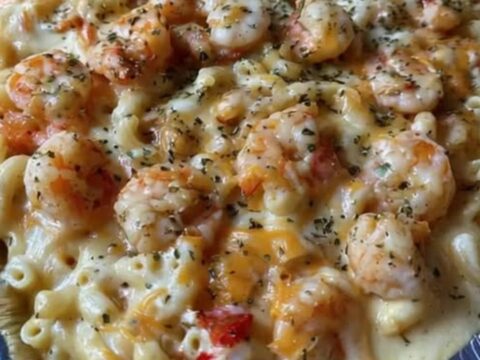 A golden, bubbling seafood mac and cheese bake in a foil pan with melted cheese and shrimp visible.