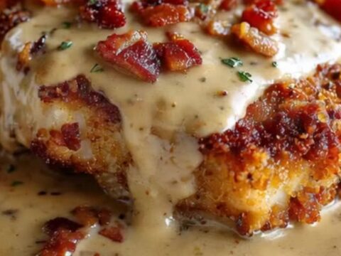 A golden-brown crispy pork chop on a white plate, generously topped with a thick, creamy bacon gravy and crispy bacon bits.