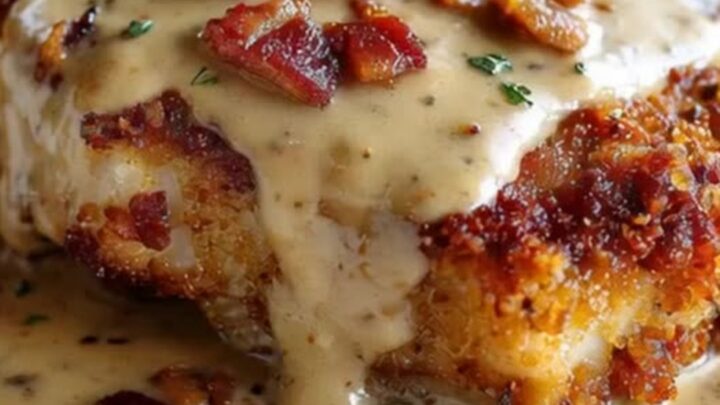 A golden-brown crispy pork chop on a white plate, generously topped with a thick, creamy bacon gravy and crispy bacon bits.