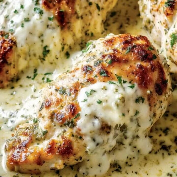 Golden-brown chicken breasts in a creamy sauce inside a dark cast iron skillet.