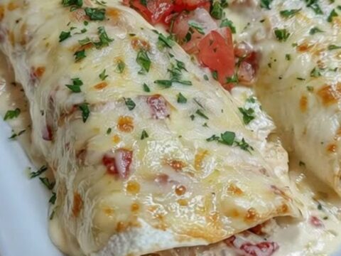 A cheesy white queso chicken enchilada being lifted from a baking dish with a metal spatula.