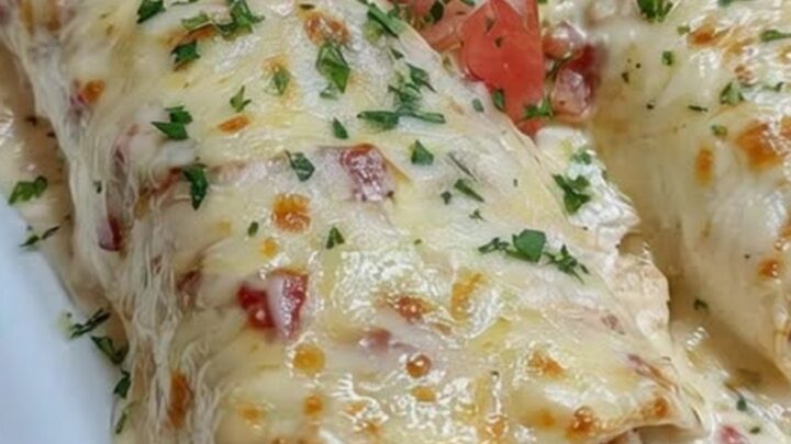 Two golden, bubbly queso chicken enchiladas served on a white platter, garnished with diced tomatoes and fresh cilantro.