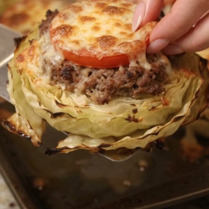 A close-up of a perfectly roasted cabbage round topped with browned ground beef and melted bubbly mozzarella cheese.