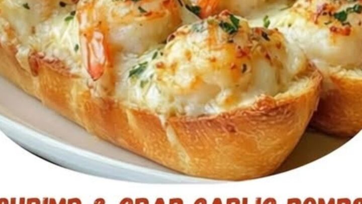 A crispy loaf of garlic bread topped with melted cheese and whole shrimp on a baking sheet.