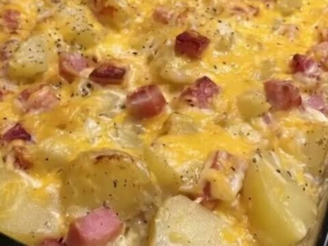 A close-up of a cheesy ham and potato casserole in a glass dish with a golden melted cheese top and steam rising.