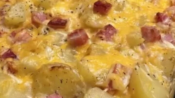 A close-up of a cheesy ham and potato casserole in a glass dish with a golden melted cheese top and steam rising.
