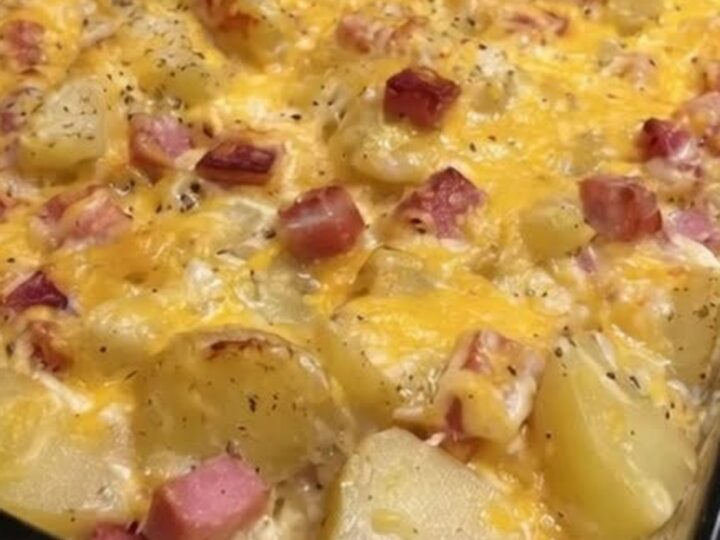 A close-up of a cheesy ham and potato casserole in a glass dish with a metal spatula lifting a portion.